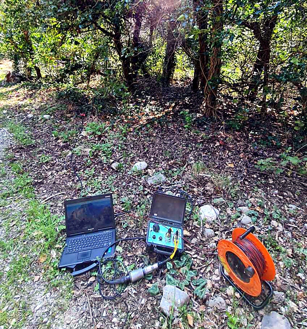The seismograph, laptop and cable reel set up on a wooded slope below the dam